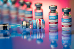 Close up of Covid-19 vaccine – vials and syringe. Glass bottles on a reflective surface